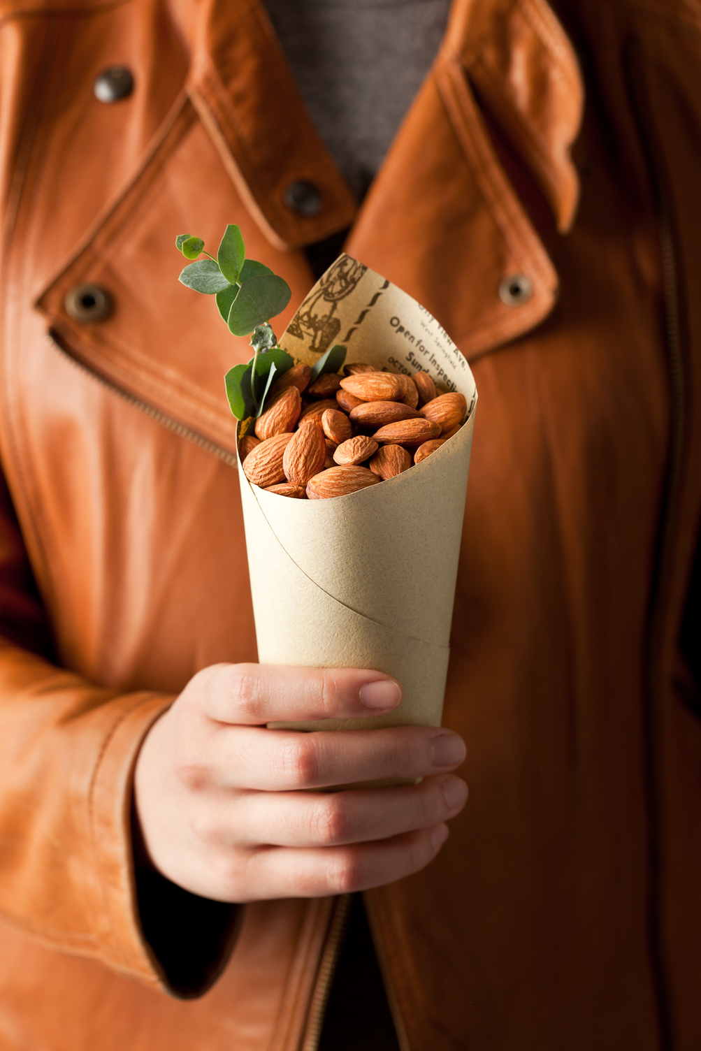 Hand holding a paper cone filled with almonds and greenery